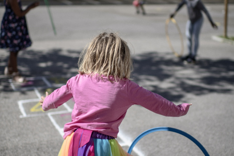 Petite fille de maternelle qui joue avec un cerceau dans la cours de récréation