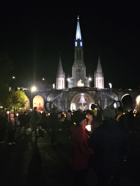 Basilique Notre Dame du Rosaire illuminée à Lourdes avec des pèlerins.