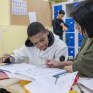 Un jeune est en train de faire ses devoirs, accompagnée d'une jeune femme dans une salle de classe